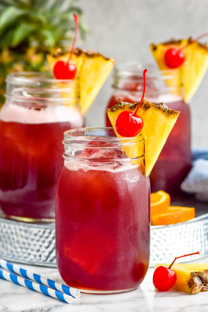 three glasses of Rum Runner with ice, garnished with fresh pineapple wedge and a cherry