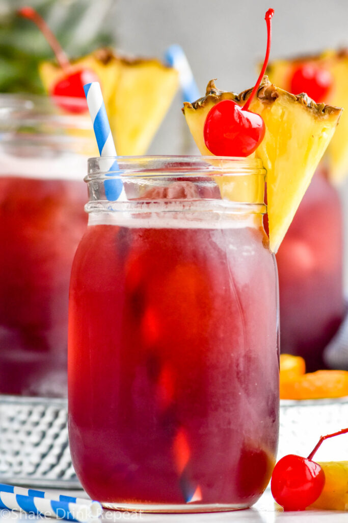 three glasses of Rum Runner with ice, garnished with fresh pineapple wedge, a cherry, and a straw