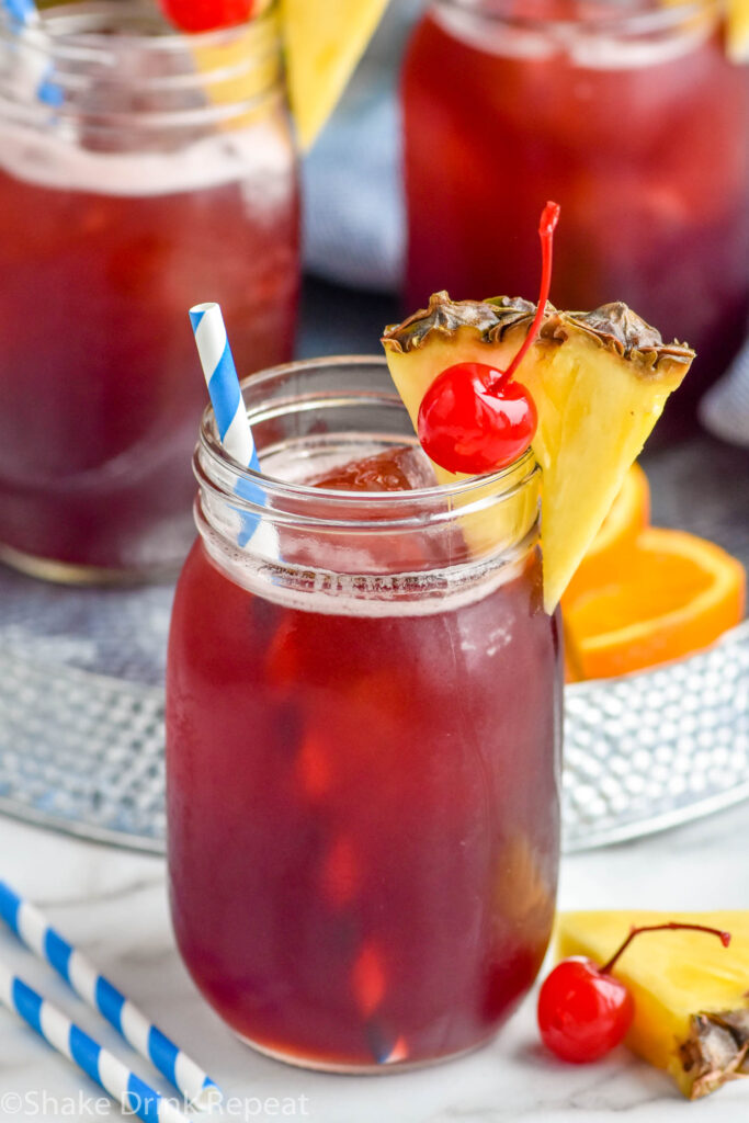 three glasses of Rum Runner with ice, garnished with fresh pineapple wedge, a cherry, and a straw