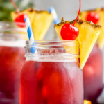 three glasses of Rum Runner with ice, garnished with fresh pineapple wedge, a cherry, and a straw