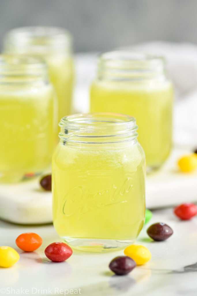 four shot glasses of Skittles Shot recipe surrounded by Skittles candy