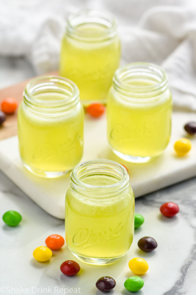 four shot glasses of Skittles Shot recipe surrounded by Skittles candy