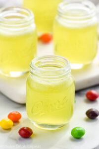 four shot glasses of Skittles Shot recipe surrounded by Skittles candy