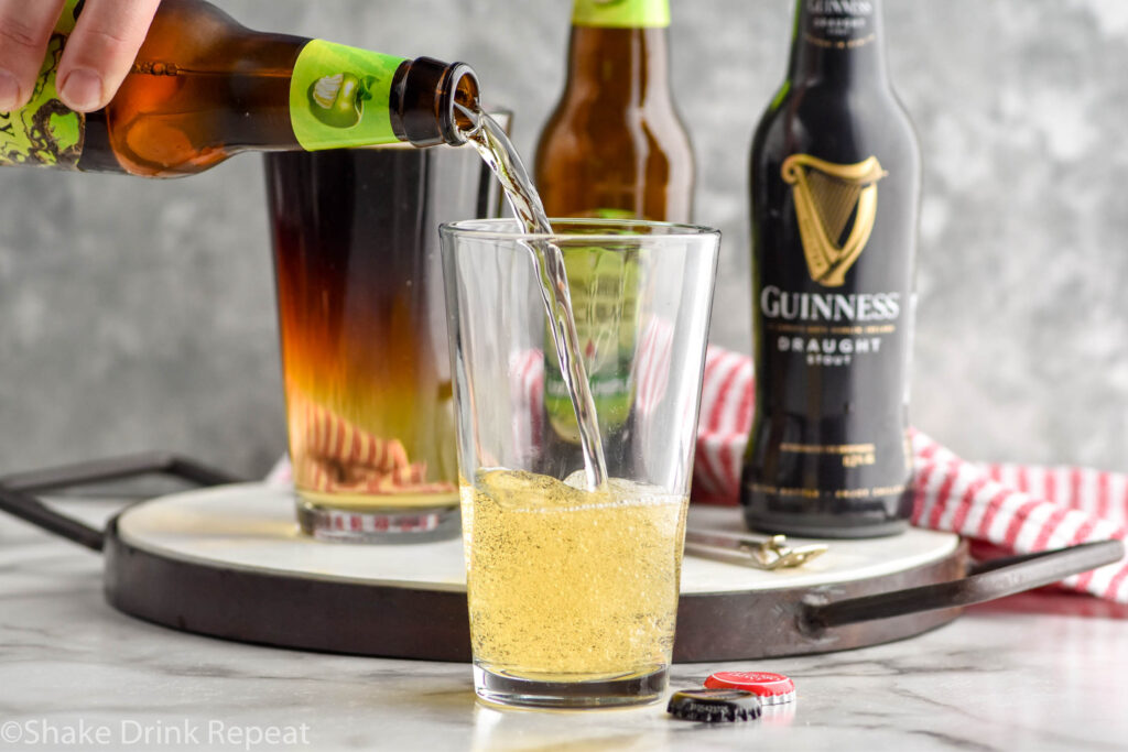 man's hand pouring bottle of hard cider into a pint glass to make a Snakebite