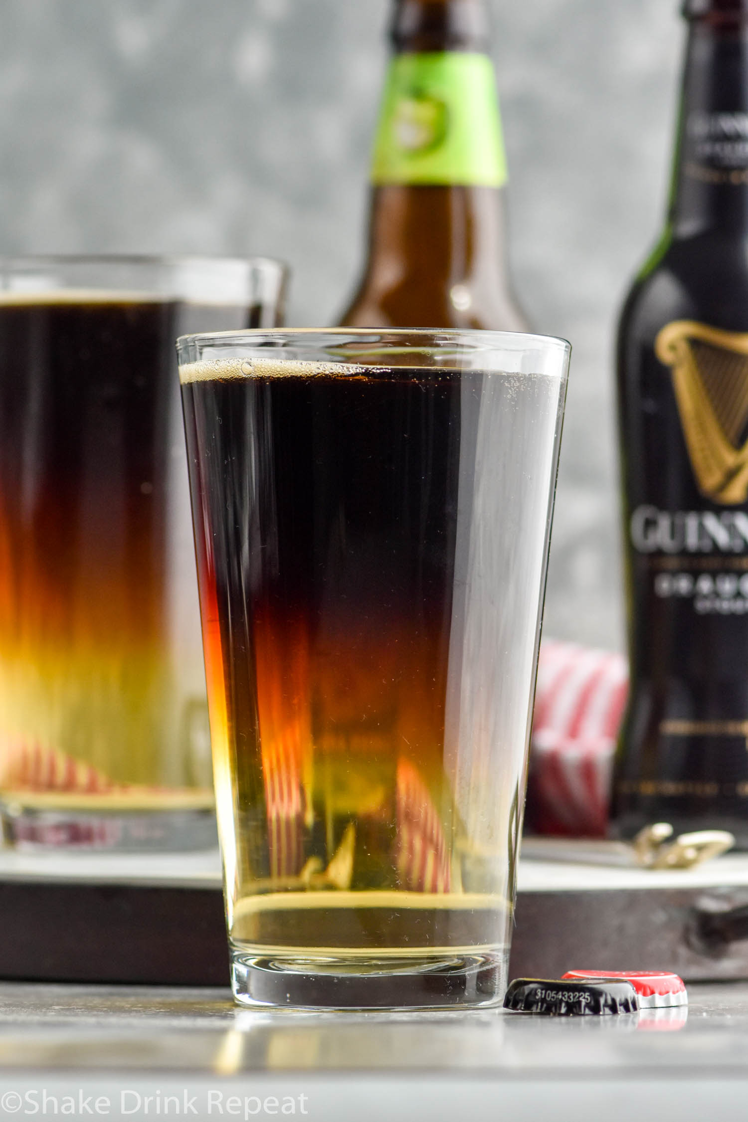 two pint glasses of Snakebite drink with bottles of hard cider and Guinness in the background