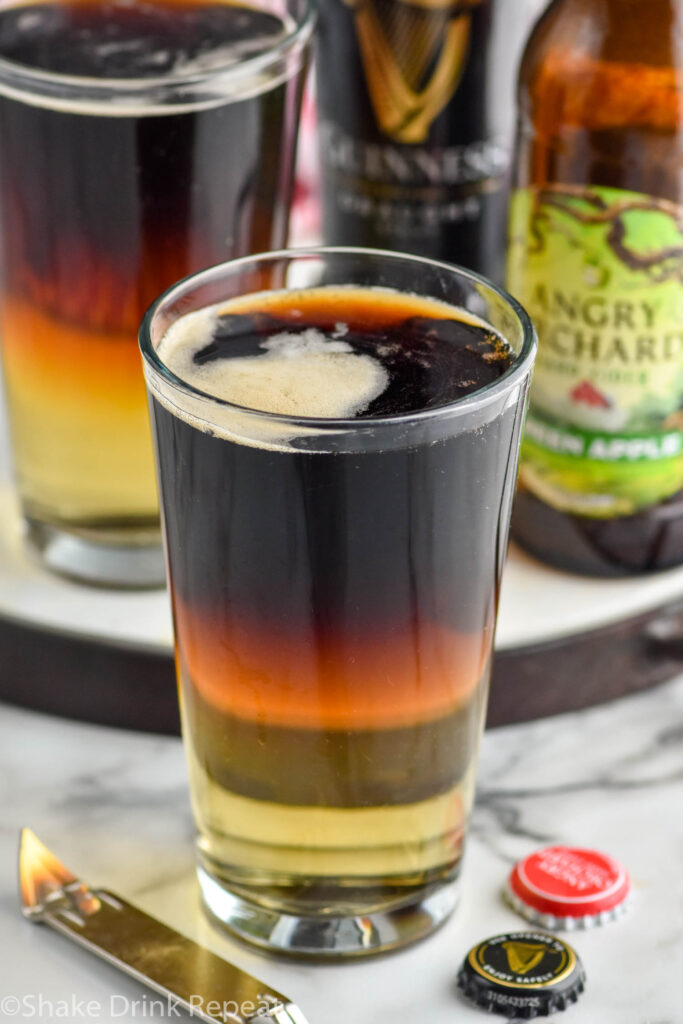 two pint glasses of Snakebite drink with bottles of hard cider and Guinness in the background