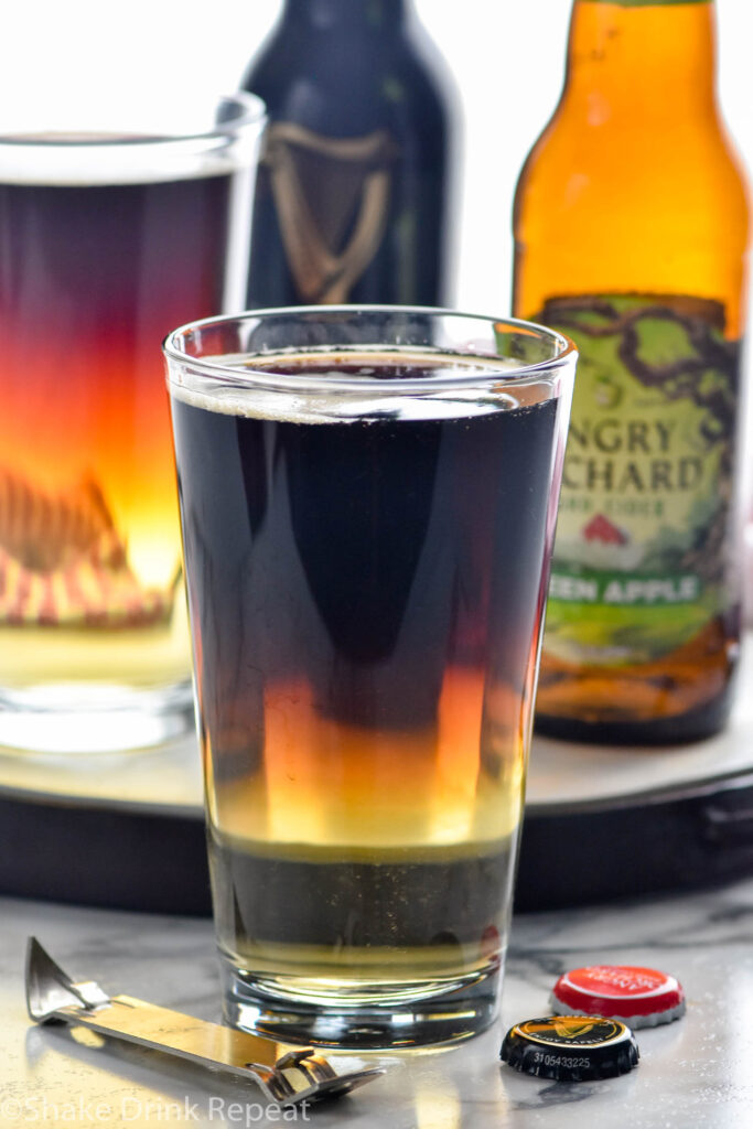 two pint glasses of Snakebite drink with bottles of hard cider and Guinness in the background