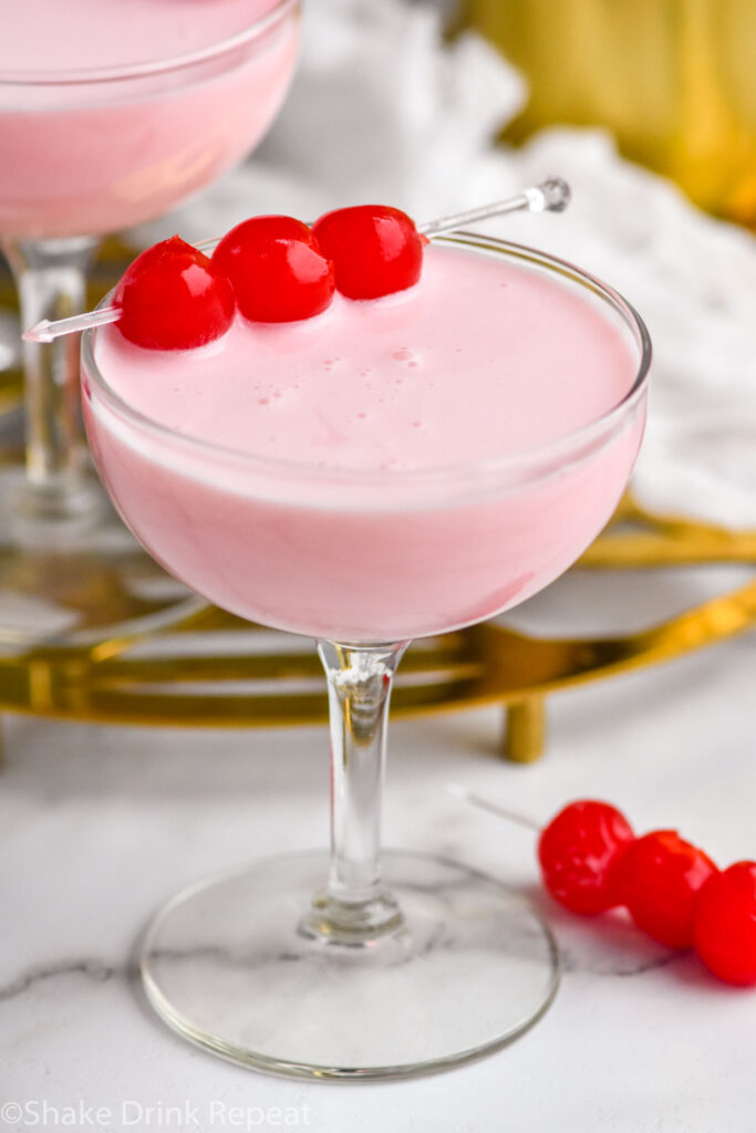 Coupe glass of Pink Squirrel cocktail garnished with maraschino cherries