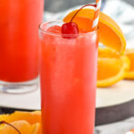 two glasses of Alabama Slammer drink with ice, garnished with a orange slice, cherry, and a straw
