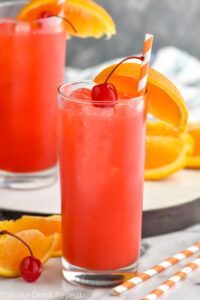 two glasses of Alabama Slammer drink with ice, garnished with a orange slice, cherry, and a straw