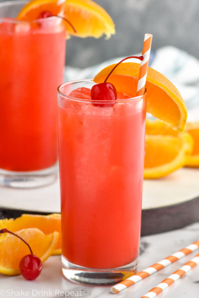 two glasses of Alabama Slammer drink with ice, garnished with a orange slice, cherry, and a straw