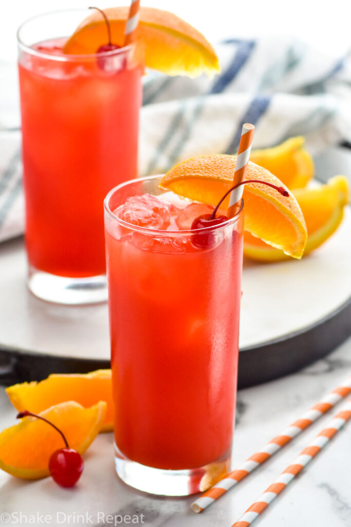 two glasses of Alabama Slammer drink with ice, garnished with a orange slice, cherry, and a straw