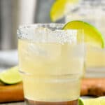 Golden margarita served in a clear glass over ice with a salted rim and lime wedge garnish.