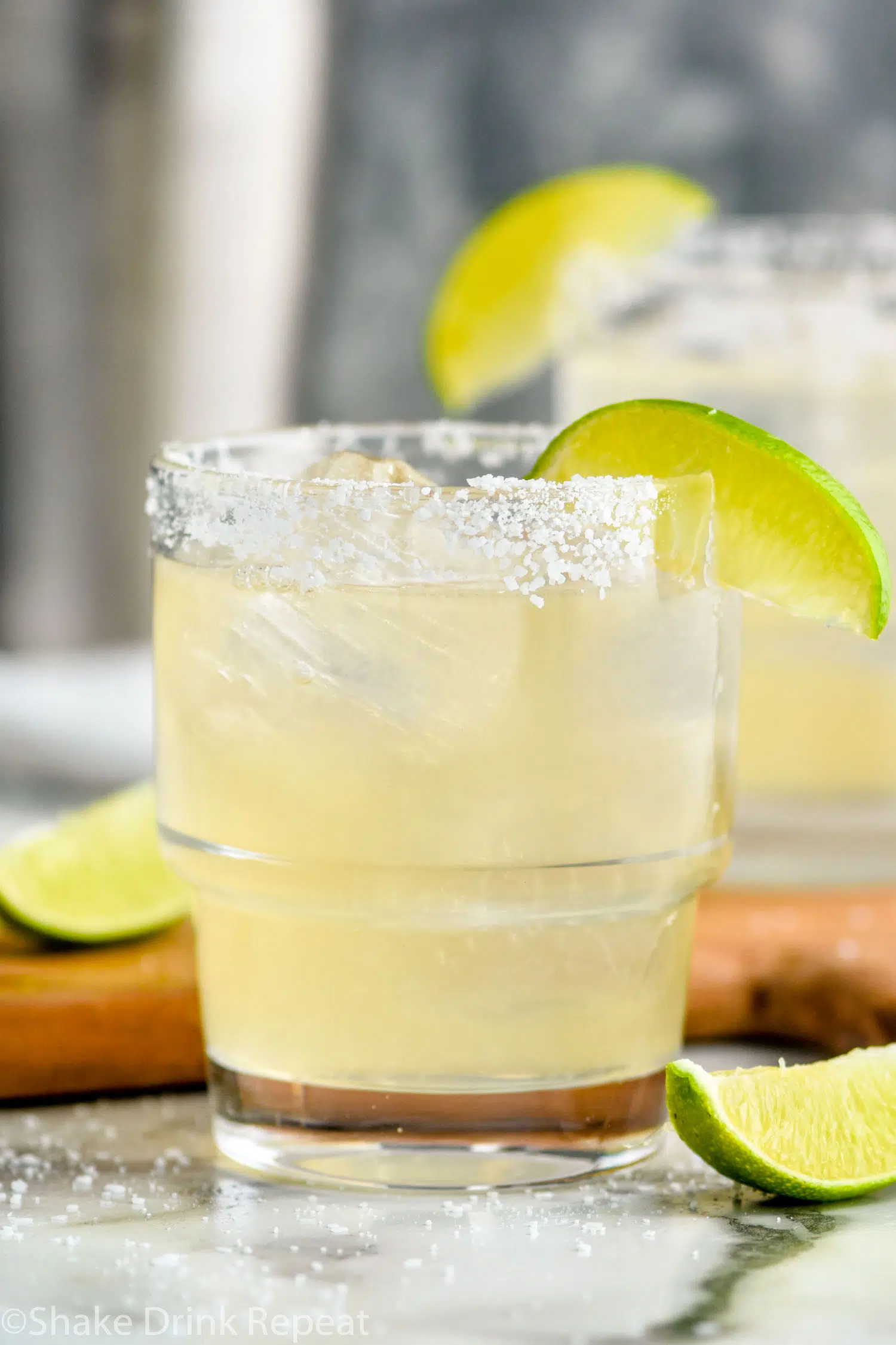 Golden margarita served in a clear glass over ice with a salted rim and lime wedge garnish.
