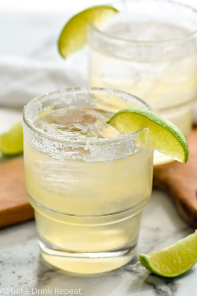 Golden margaritas served in a clear glass over ice with a salted rim and lime wedge garnish.