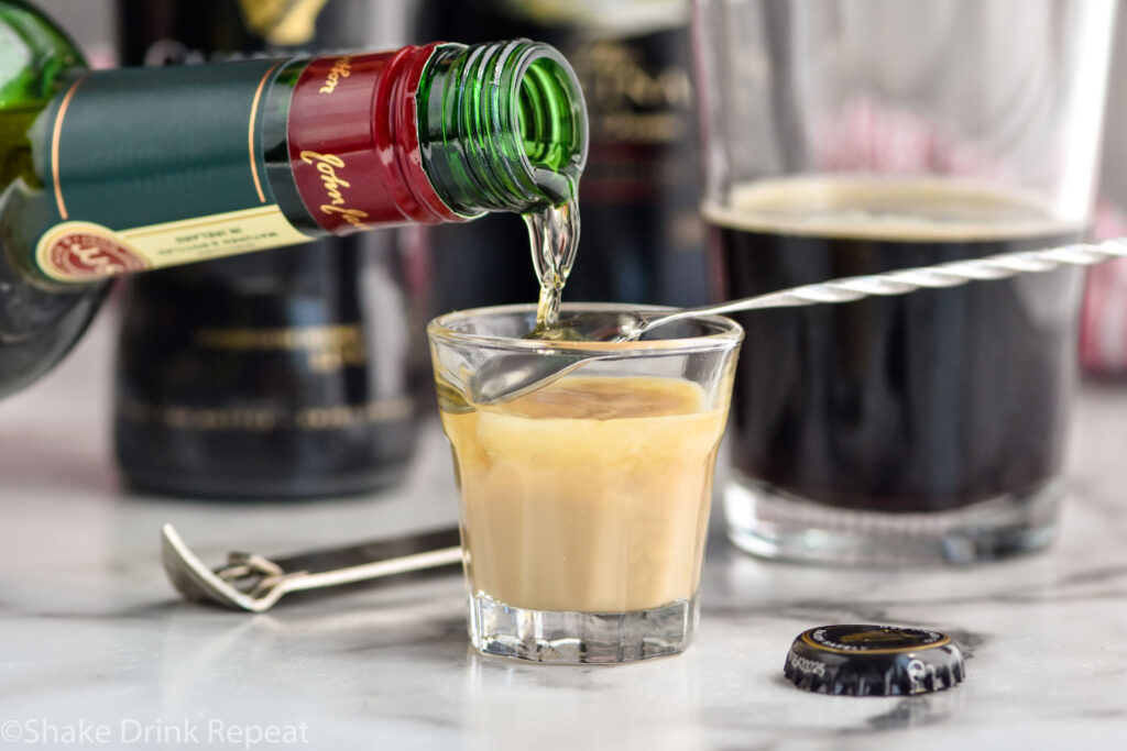 bottle of Jameson whiskey pouring over the back of a spoon into a shot glass of Baileys irish cream to make an Irish Car Bomb shot