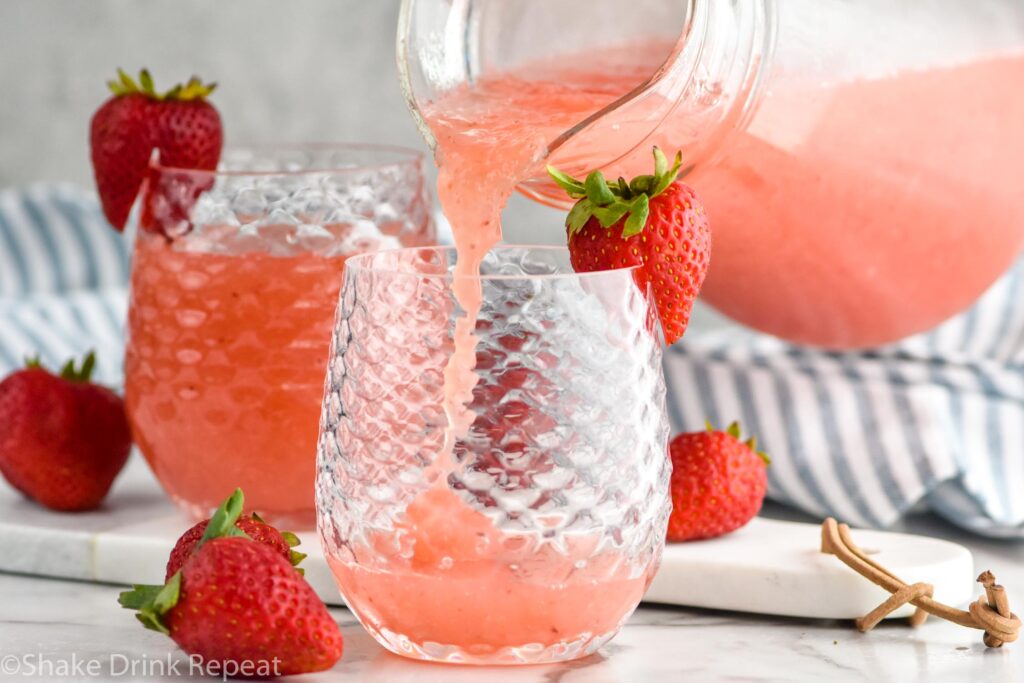 pitcher of Frose ingredients pouring into a glass garnished and surrounded by fresh strawberries