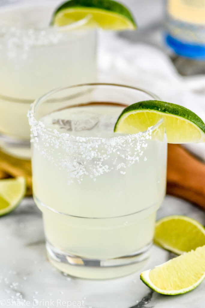 Photo of two glasses of Mezcal Margaritas garnished with salted rims and lime wedges.
