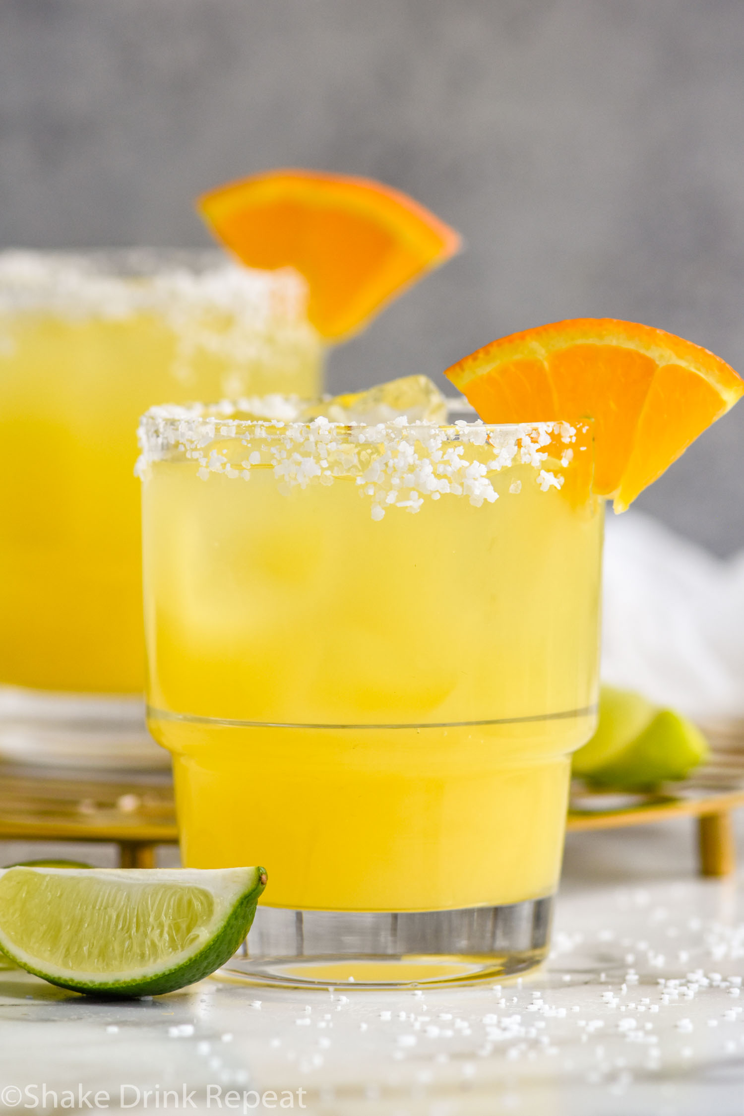 Photo of Italian Margarita recipe served in a glass with a salted rim and garnished with an orange slice. Lime wedges lay on the counter beside the glass.