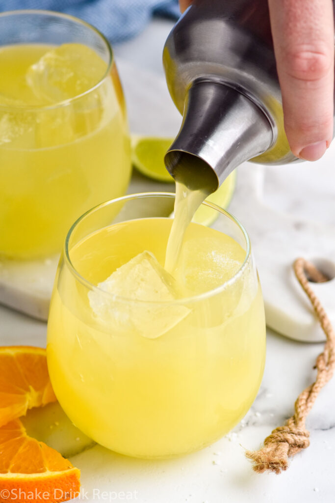 Overhead photo of man's hand pouring Texas Margarita recipe from a shaker bottle into a glass of ice.