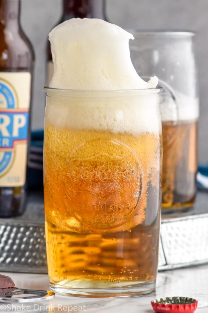 shot glass of whiskey dropping into a glass of beer to make a boilermaker drink with boilermaker and two bottles of beer sitting in background