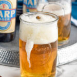 shot glass of whiskey dropping into a glass of beer to make a boilermaker drink with boilermaker and two bottles of beer sitting in background