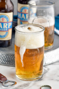 shot glass of whiskey dropping into a glass of beer to make a boilermaker drink with boilermaker and two bottles of beer sitting in background