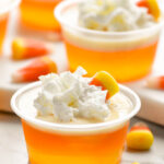 shot glasses of candy corn jello shots topped with whipped cream and candy corn candy