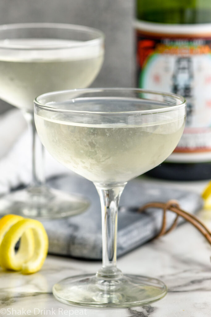 two glasses of saketini recipe with a lemon twist beside and a bottle of sake in the background