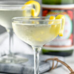 two glasses of saketini recipe garnished with a lemon twist with bottle of sake in the background