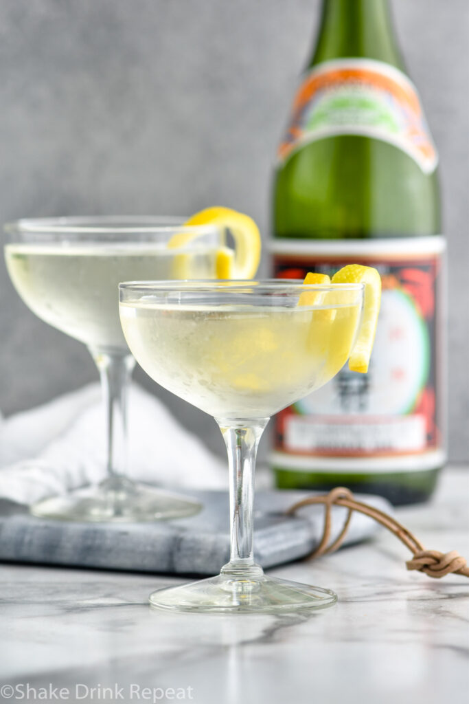 two glasses of saketini recipe garnished with a lemon twist with bottle of sake in the background