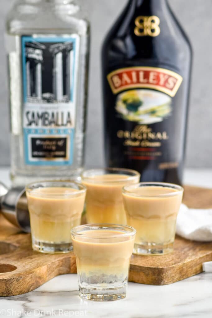 four shot glasses of slippery nipple with bottles of Bailey's irish cream and sambuca sitting in background