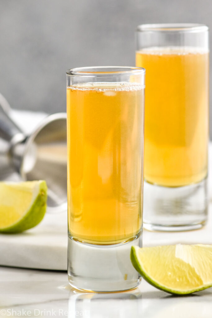 two shot glasses of snakebite shot recipe surrounded by lime wedges