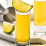 two shot glasses of snakebite shot recipe garnished with lime wedges