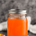 Pinterest graphic of Candy Corn Vodka. Text says "The best candy corn vodka only uses 2 simple ingredients shakedrinkrepeat.com" Image shows mason jar of candy corn vodka with candy corns surrounding.