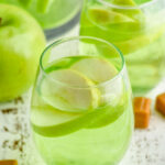 two wine glasses of caramel apple sangria with fresh apple slices, surrounded by caramel candies