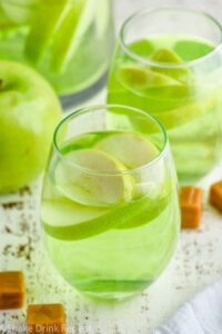 two wine glasses of caramel apple sangria with fresh apple slices, surrounded by caramel candies