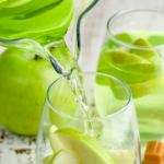 Pinterest graphic of caramel apple sangria. Text says "the best caramel apple sangria only uses 4 simple ingredients! shakedrinkrepeat.com" Image shows pitcher of caramel apple sangria pouring into a wine glass of fresh apple slices surrounded by caramel candies