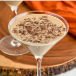 pinterest graphic of pumpkin spice mudslide recipe. Text says "the best pumpkin spice mudslide shakedrinkrepeat.com" Image shows martini glass of pumpkin spice mudslide topped with chocolate shavings. Cinnamon sticks lay beside.