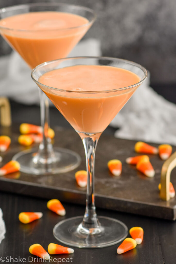 Two martini glasses of candy corn martini. Candy corn surrounding base of glasses.