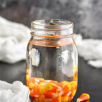 Mason jar of candy corn vodka with candy corn candies surrounding jar