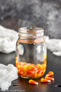 Mason jar of candy corn vodka with candy corn candies surrounding jar
