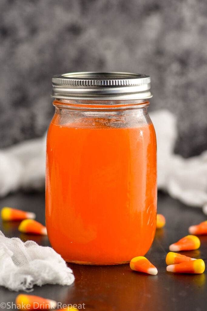 Mason jar of candy corn vodka with candy corn candies surrounding jar