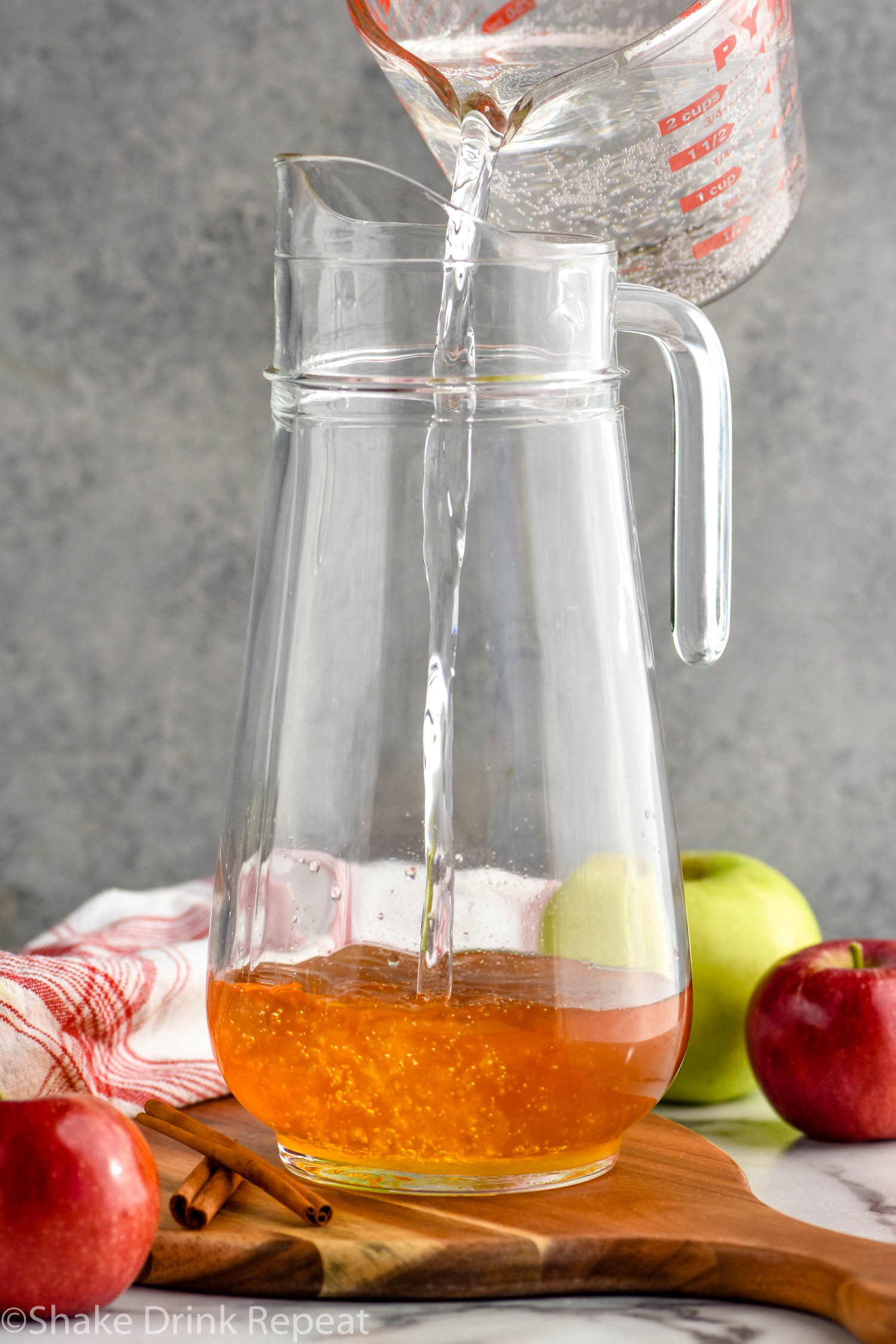 glass measuring cup pouring lemon-lime soda into a glass picture with fireball whiskey to make a fireball whiskey bunch. Fresh apples and cinnamon sticks sit beside.