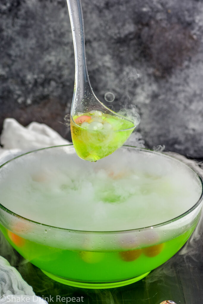 ladle holding scoop of Halloween punch over punch bowl of Halloween punch with dry ice and eye ball garnish