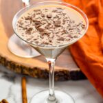 overhead view of two martini glasses of pumpkin spice mudslide garnished with chocolate shavings. Cinnamon sticks lay beside.