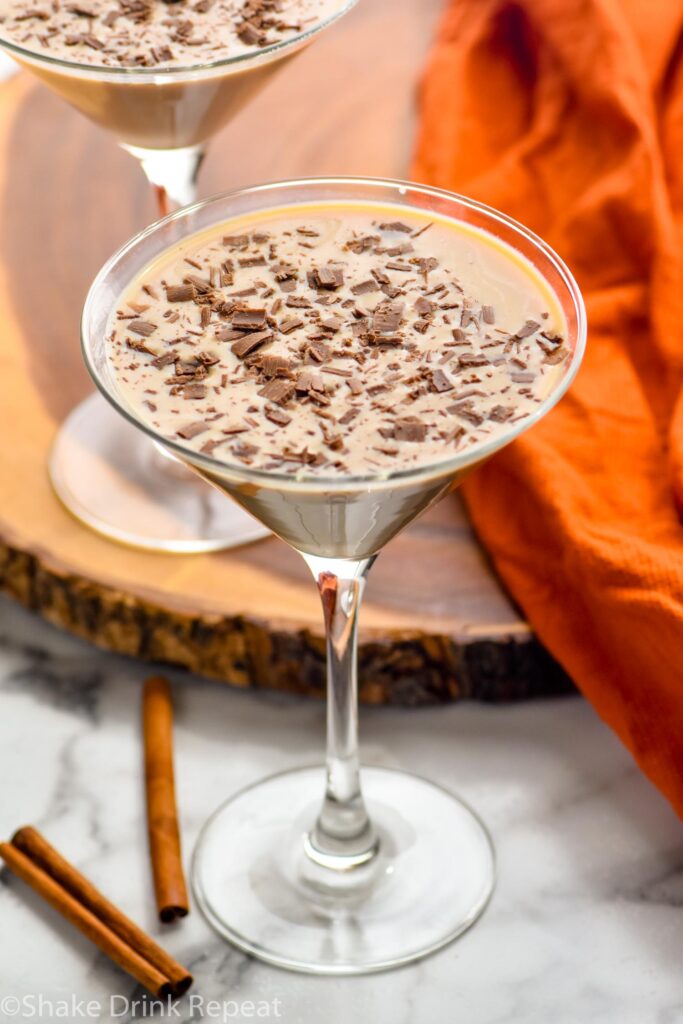 overhead view of two martini glasses of pumpkin spice mudslide garnished with chocolate shavings. Cinnamon sticks lay beside.