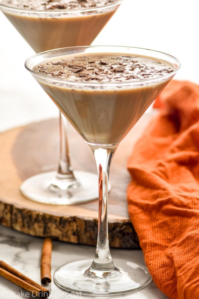 two martini glasses of pumpkin spice mudslide garnished with chocolate shavings. Cinnamon sticks lay beside.