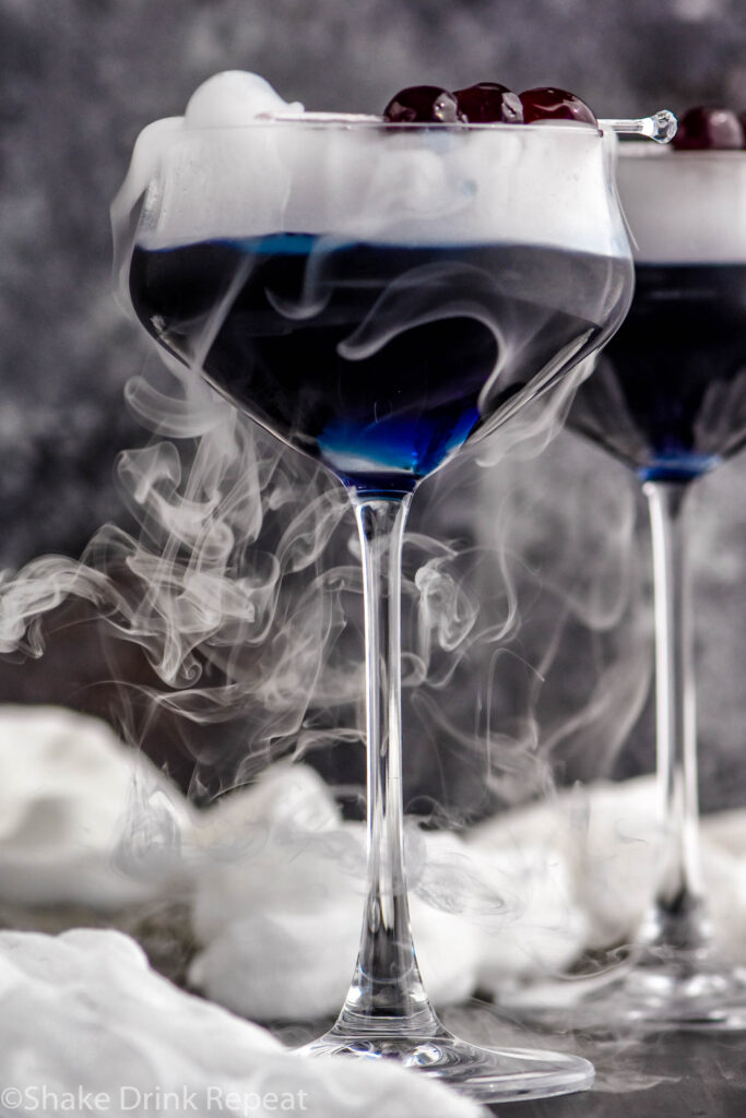 two glasses of witches brew cocktails garnished with dark cherries and dry ice