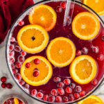 Pinterest graphic of Christmas Punch. Text says "the best Christmas punch shakedrinkrepeat.com" Image shows an overhead view of a bowl of Christmas punch garnished with orange slices and cranberries.